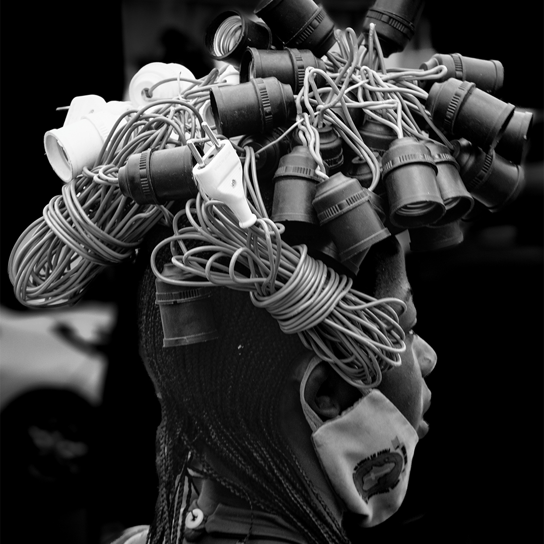 Fotografia artística em preto e branco de uma mulher Himba com adereços tradicionais em perfil, destacando o tema 'Traços de [es]culturas'.